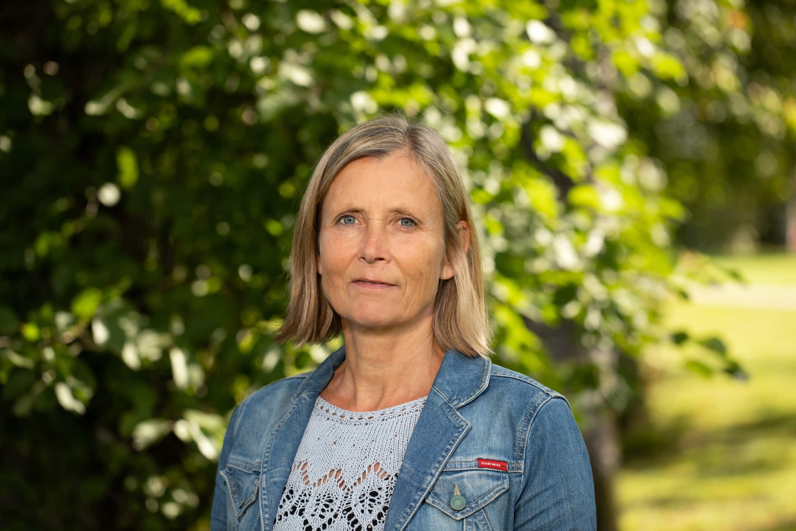Bilde av Siw Heggedal Longvast&oslash;l, som er avdelingsdirekt&oslash;r i Stiftelsestilsynet. Hun st&aring;r fremfor gr&oslash;nne tr&aelig;r, i en dongerijakke og gr&aring; topp.